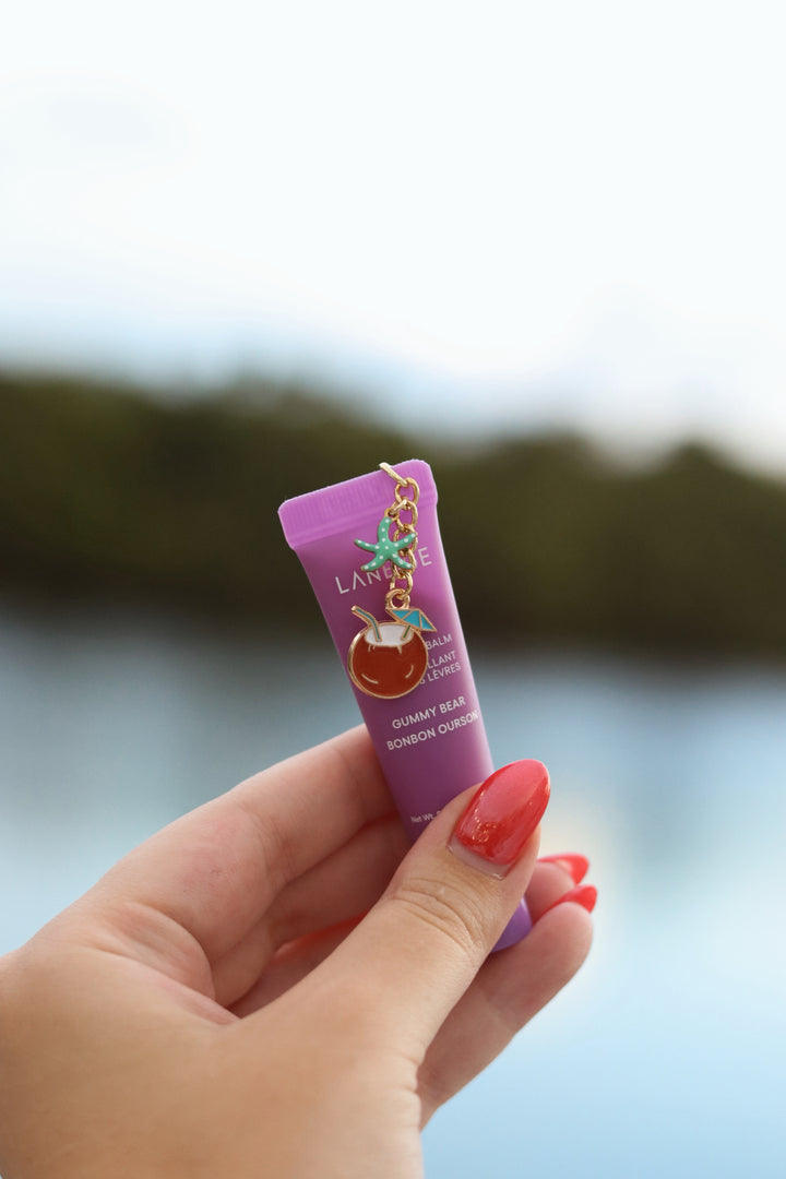 Hand holding a pink lip balm with a blurred natural background