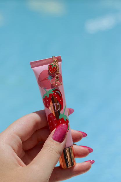Hand holding a pink lip balm with strawberry design against a blue sky background
